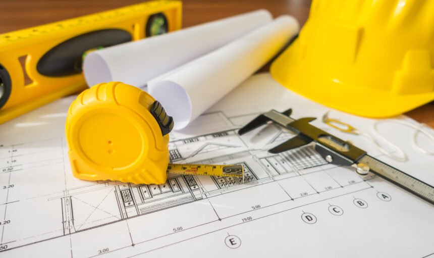 Construction plans with yellow helmet and drawing tools on blueprints